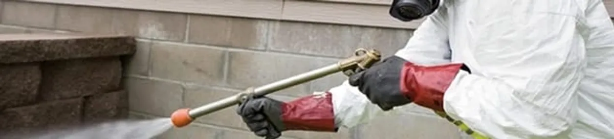 Pest control technician applying exterior insect treatment along a home foundation in Cleveland, OH