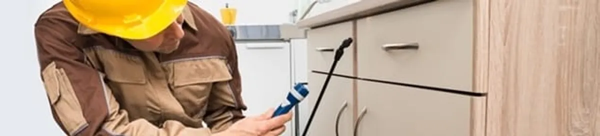 Roach exterminator applying treatment under kitchen cabinets in Cleveland, OH
