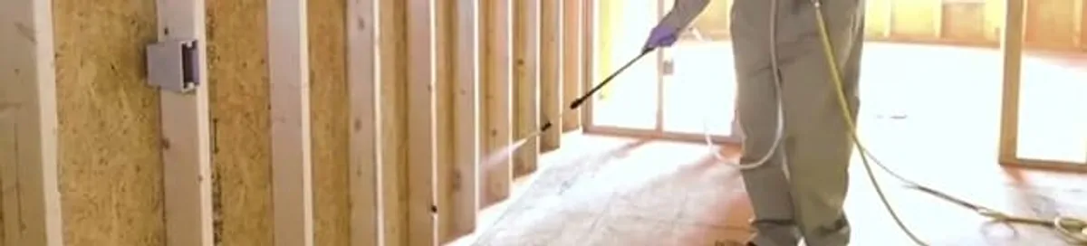Termite treatment technician applying spray along framing and unfinished walls in Cleveland, OH