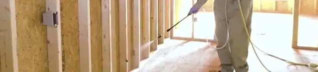 Termite treatment technician applying spray along framing and unfinished walls in Cleveland, OH